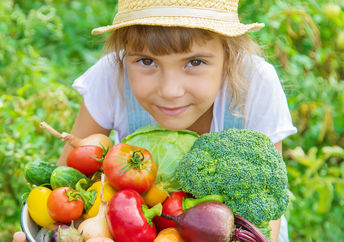 一个年轻的女孩在田野里提着一个装满新鲜采摘的蔬菜的篮子。